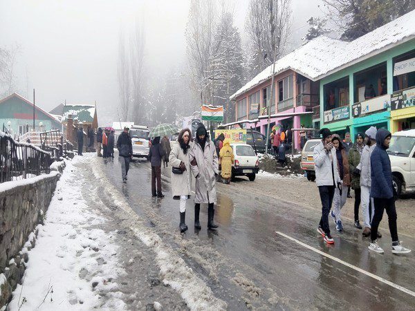 Baramulla, Nov 14, (ANI): Tourists walk on the snow-covered road toward the Gulmarg Ski Resort as higher reaches of the Kashmir valley receives fresh snowfall, at Tangmarg, in Baramulla on Monday. (ANI Photo)