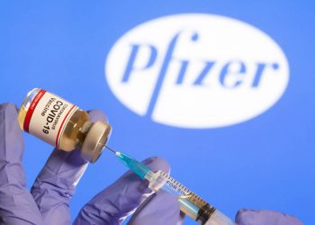 FILE PHOTO: A woman holds a small bottle labeled with a "Coronavirus COVID-19 Vaccine" sticker and a medical syringe in front of displayed Pfizer logo in this illustration taken, October 30, 2020. REUTERS/Dado Ruvic/File Photo