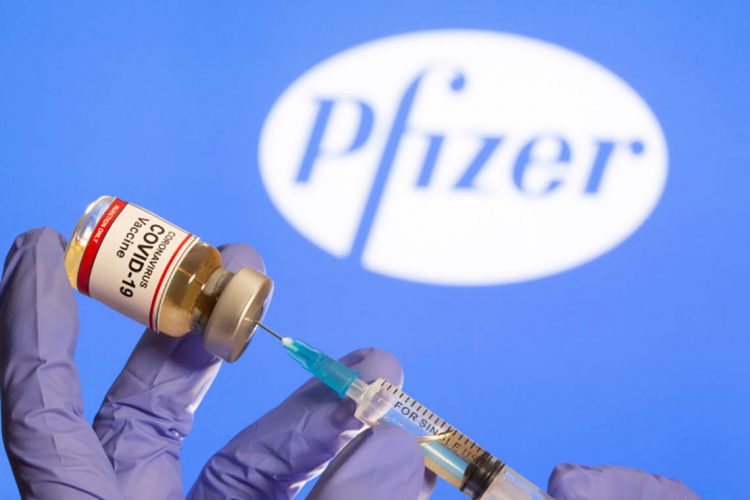 FILE PHOTO: A woman holds a small bottle labeled with a "Coronavirus COVID-19 Vaccine" sticker and a medical syringe in front of displayed Pfizer logo in this illustration taken, October 30, 2020. REUTERS/Dado Ruvic/File Photo