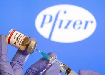 FILE PHOTO: A woman holds a small bottle labeled with a "Coronavirus COVID-19 Vaccine" sticker and a medical syringe in front of displayed Pfizer logo in this illustration taken, October 30, 2020. REUTERS/Dado Ruvic/File Photo