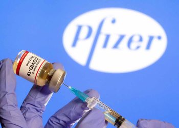 FILE PHOTO: A woman holds a small bottle labeled with a "Coronavirus COVID-19 Vaccine" sticker and a medical syringe in front of displayed Pfizer logo in this illustration taken, October 30, 2020. REUTERS/Dado Ruvic//File Photo
