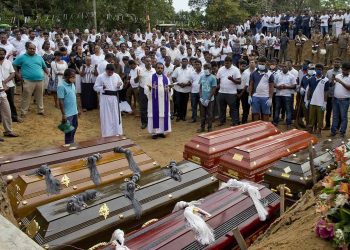 A priest conducts religious rituals during a mass burial for Easter Sunday bomb blast victims in Negombo, Sri Lanka, Wednesday, April 24, 2019. (AP Photo/Gemunu Amarasinghe)