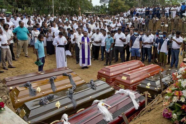 A priest conducts religious rituals during a mass burial for Easter Sunday bomb blast victims in Negombo, Sri Lanka, Wednesday, April 24, 2019. (AP Photo/Gemunu Amarasinghe)