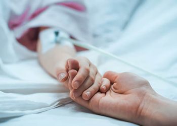 Recovering Little Child Lying in the Hospital Bed Sleeping, Mother Holds Her Hand Comforting. Focus on the Hands. Emotional Family Moment.