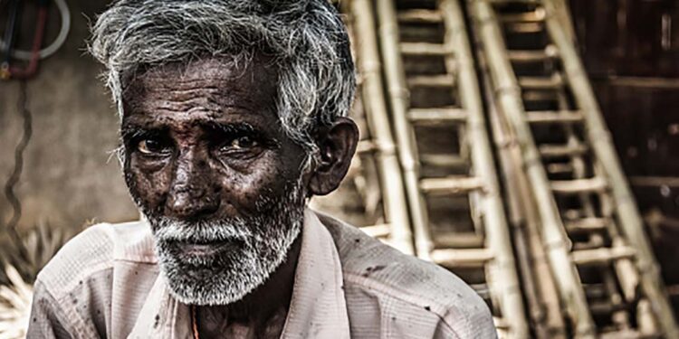 Portrait of Indian elder man with traditional bindi as a third eye, white beard and bamboo ladders on the background in Mysore, Karnataka, India. Concerned expression
