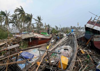 TOPSHOT - Local residents stand on broken boats in Sittwe, on May 15, 2023, after cyclone Mocha made a landfall. Cyclone Mocha made landfall between Cox's Bazar in Bangladesh and Myanmar's Sittwe carrying winds of up to 195 kilometres (120 miles) per hour, the biggest storm to hit the Bay of Bengal in more than a decade. (Photo by Sai Aung MAIN / AFP)