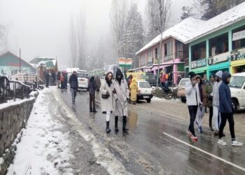 Baramulla, Nov 14, (ANI): Tourists walk on the snow-covered road toward the Gulmarg Ski Resort as higher reaches of the Kashmir valley receives fresh snowfall, at Tangmarg, in Baramulla on Monday. (ANI Photo)
