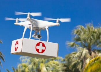 Unmanned Aircraft System (UAS) Quadcopter Drone Carrying First Aid Package Over Tropical Terrain.