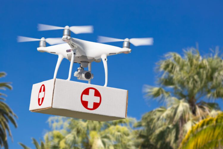 Unmanned Aircraft System (UAS) Quadcopter Drone Carrying First Aid Package Over Tropical Terrain.