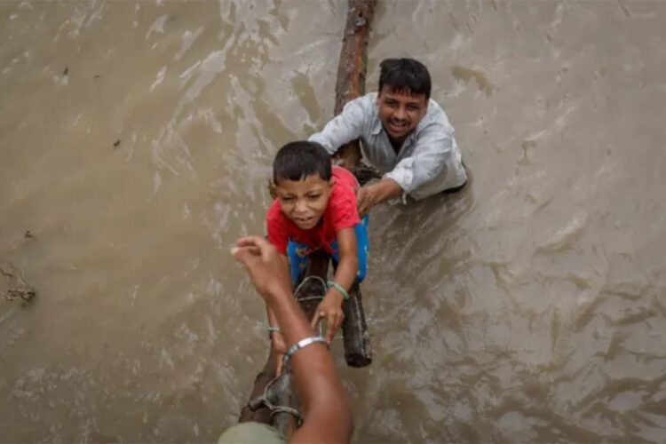 නවදිල්ලියේ යමුනා ගඟේ ජල මට්ටම ඉහළ යාමෙන් අවතැන් වීමෙන් පසු ඉදිවෙමින් පවතින ගුවන් පාලමකට නැගීමට පියකු තම පුතාට උදව් කරන අයුරු [අඩ්නාන් අබිඩි/රොයිටර්]