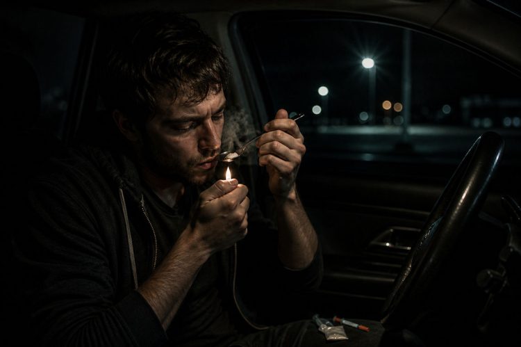 person sitting in the driver's seat on a dark background and smoking heroin